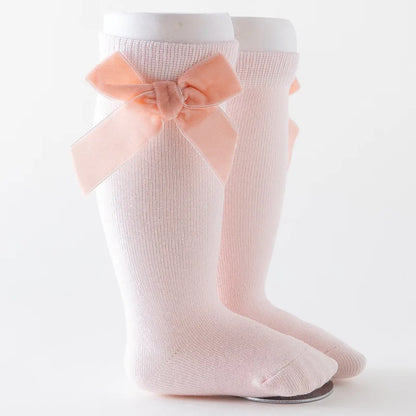 Detailed view of the elastic cuff and bow knot on a baby girl's light pink knee-high sock.