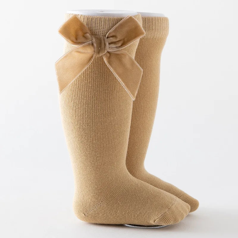 Baby girl's legs with white knee-high bow socks paired with cute Mary Jane shoes.