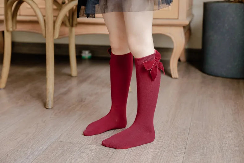 Infant girl's knee-high socks in a classic black color, adorned with a sophisticated bow.