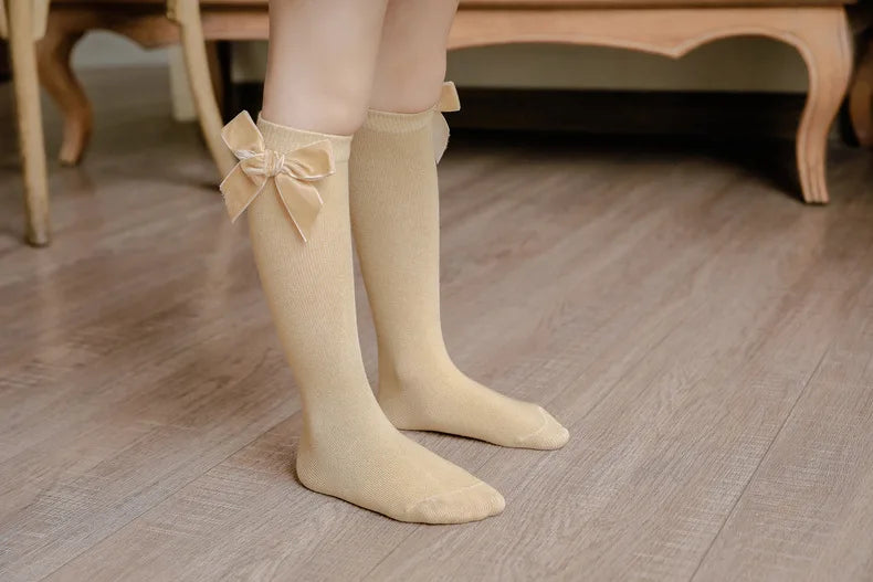 Toddler girl's outfit detail: White dress with delicate knee-high bow socks for a special occasion.
