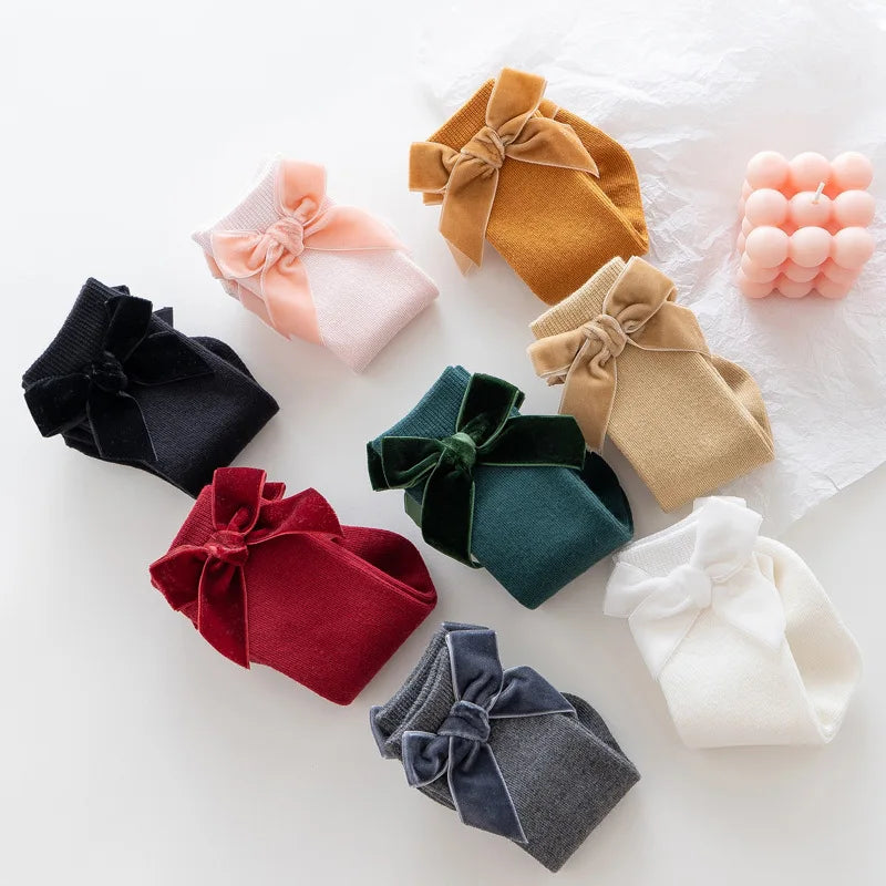 Close-up of a baby girl's knee-high sock showing a detailed fabric bow and soft cotton blend.