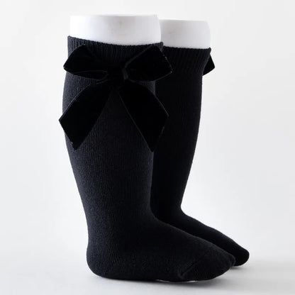 Stylish baby girl's knee-high socks with a fuchsia bow, adding a pop of color to outfits.
