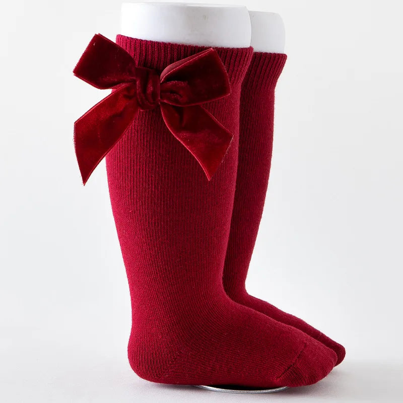 Soft knit knee-high infant socks in a cream color with an understated, sweet bow.