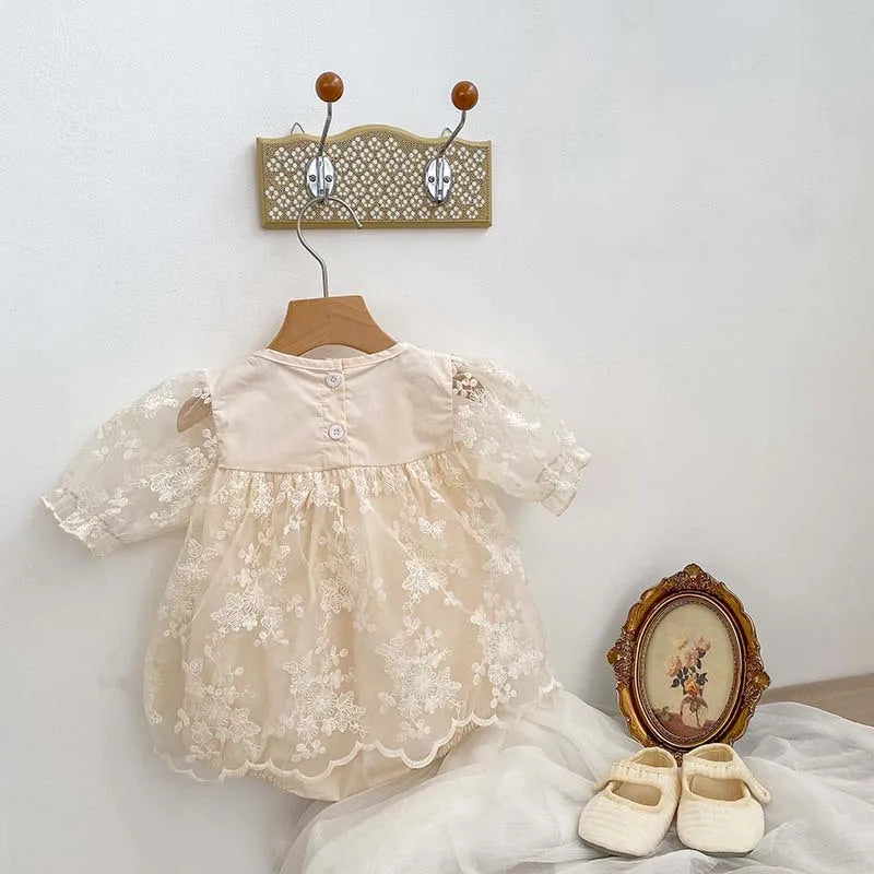 Close-up of soft cotton fabric and detailed lace embroidery on a baby girl's summer bodysuit.