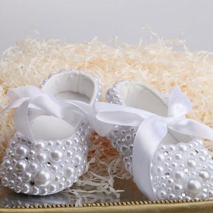 Close-up of baby girl's pearl and ribbon first walker shoes, perfect for special occasions.