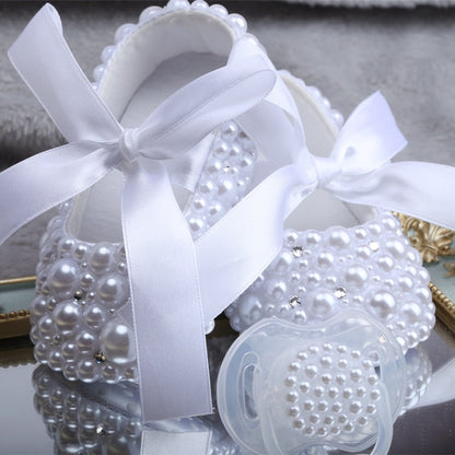 Elegant baby girl's white first walker shoes with delicate pearl and ribbon accents and pacifier.