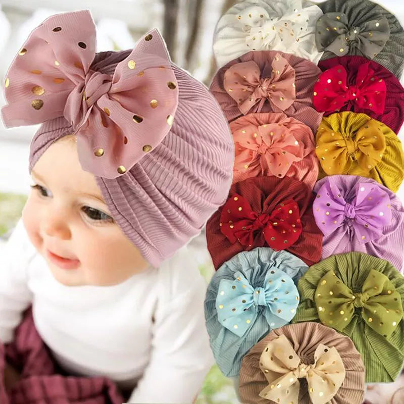 Baby girl wearing a shiny pink bowknot turban hat, soft infant headwear.