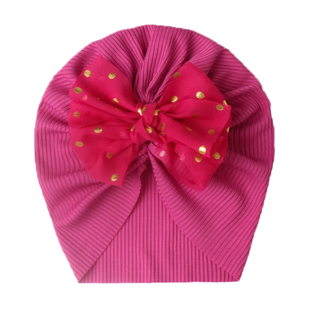 Baby girl in a vibrant shiny hot pink bowknot turban, soft headwear.