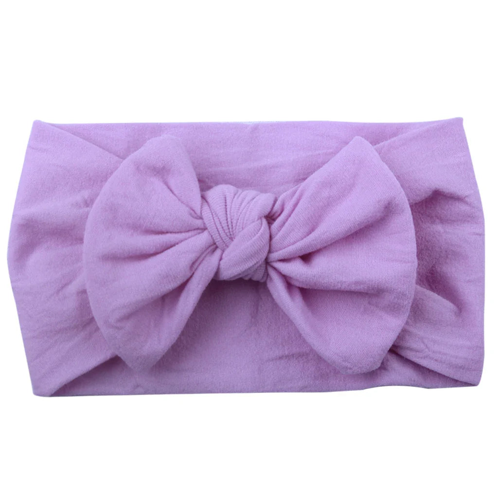 Child smiling and wearing a bright yellow bowknot headband, soft elastic fabric.