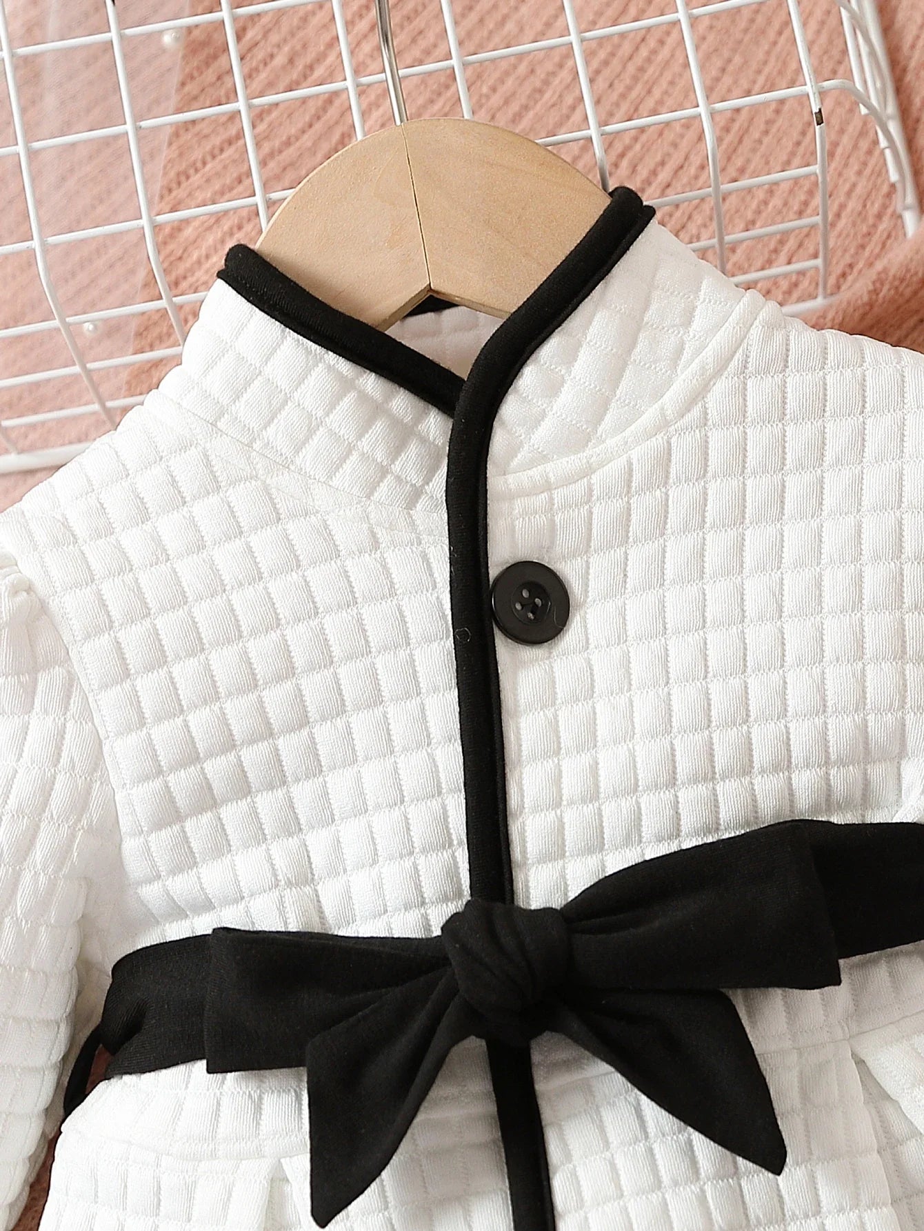 Close-up of baby girls' thermal dress with belt detail, black and white pattern, infant clothing