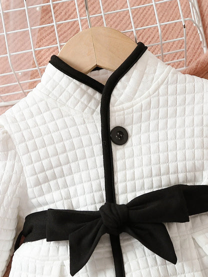 Close-up of baby girls' thermal dress with belt detail, black and white pattern, infant clothing