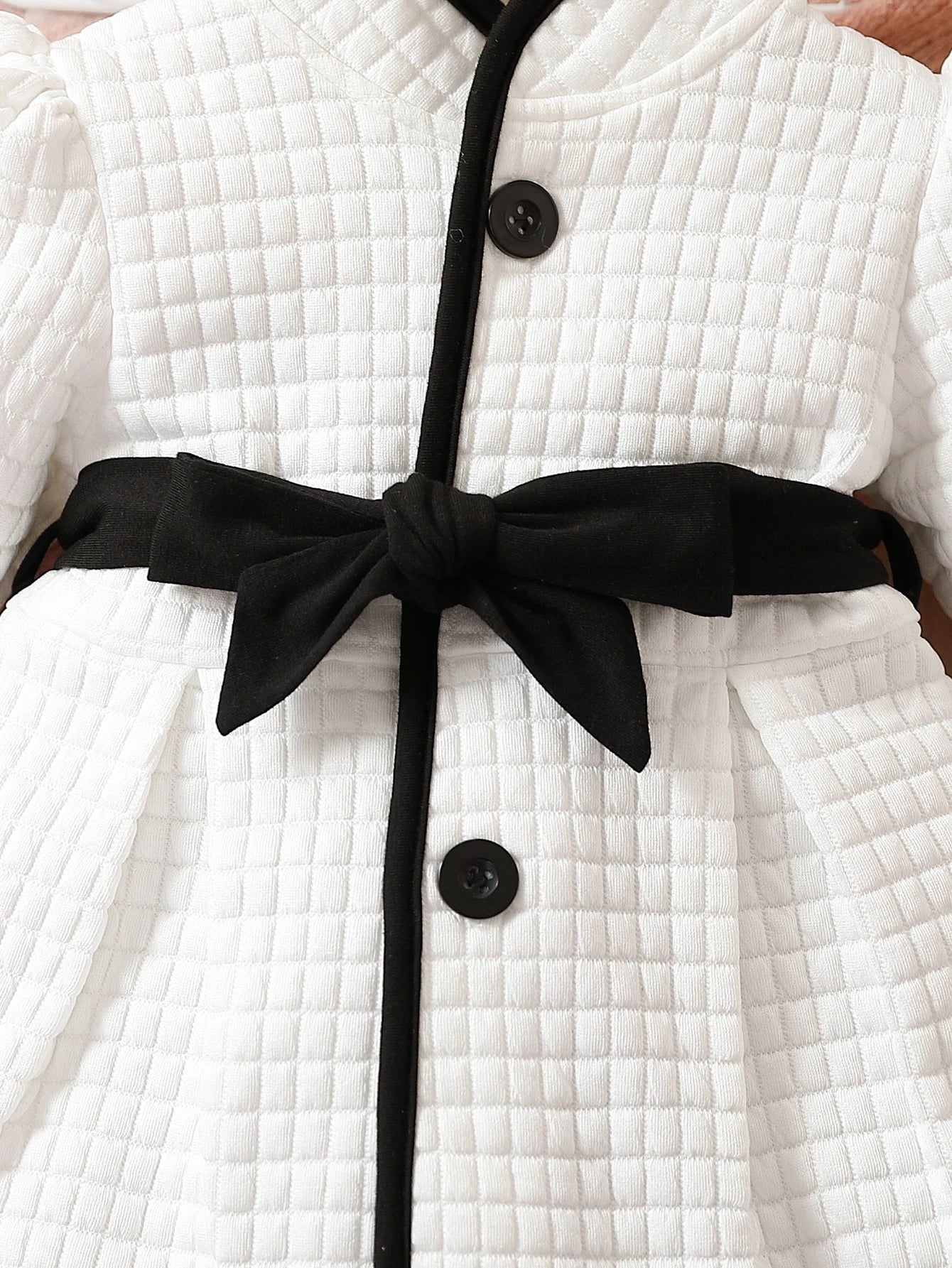 Detail of belted waist on baby girls' thermal dress, black and white print, stylish infant outfit