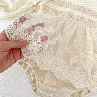 Detail shot of the lace trim on a baby girl's pink waffle knit bodysuit, enhancing puff sleeves.