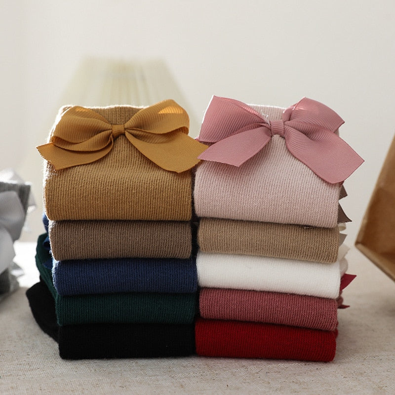 Knee-high baby girl socks with subtle patterns and a prominent bow accent, comfortable cotton