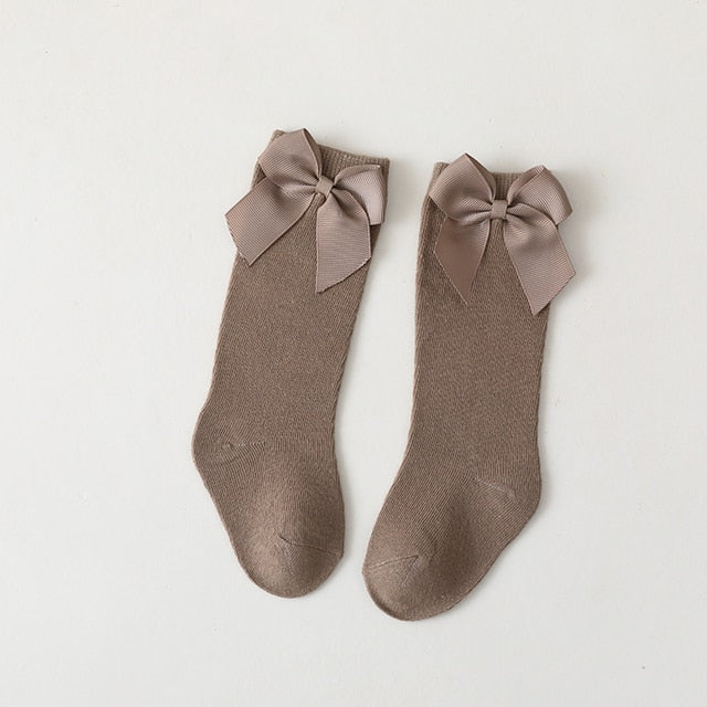 Close-up of white knee-high baby girl socks, showing detailed satin bow and knit texture
