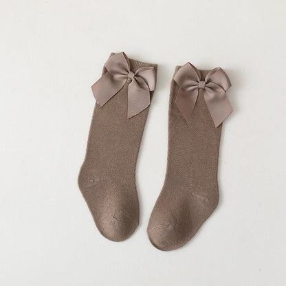 Close-up of white knee-high baby girl socks, showing detailed satin bow and knit texture