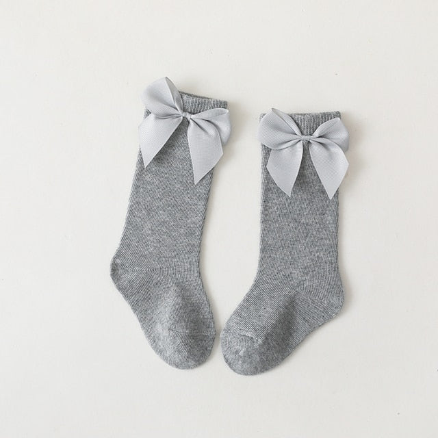 Baby wearing pink knee-high bow socks with a cute dress, suitable for special occasions