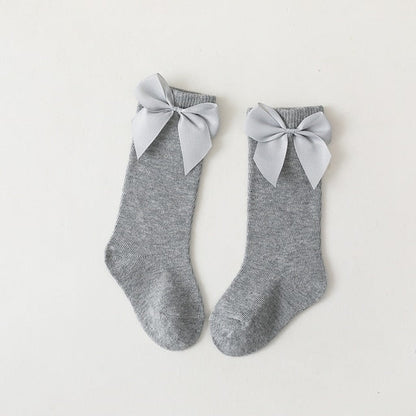 Baby wearing pink knee-high bow socks with a cute dress, suitable for special occasions