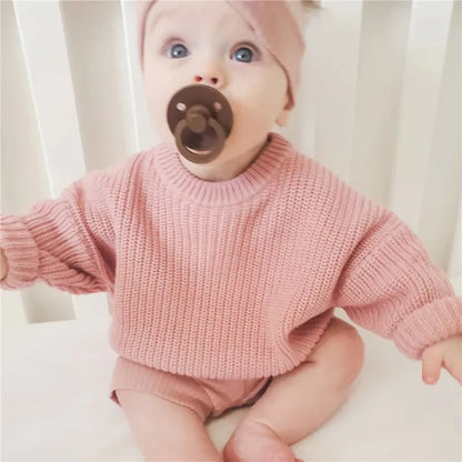 Knitted baby pullover laid next to baby toys, emphasizing it's for infant life.