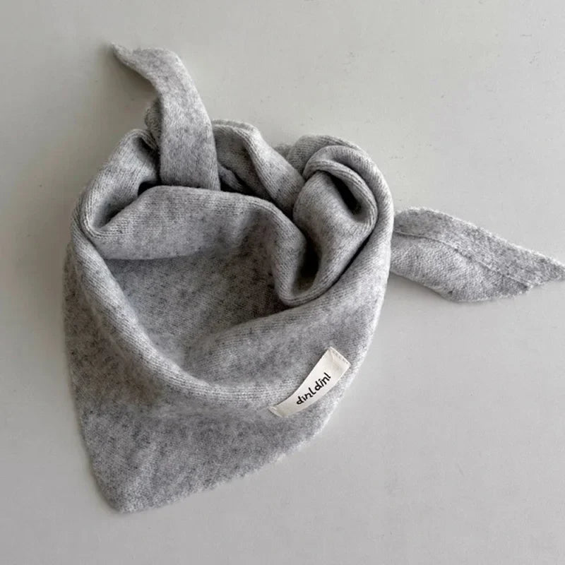 Child modeling a soft knitted triangle scarf, cozy and fashionable winter accessory.
