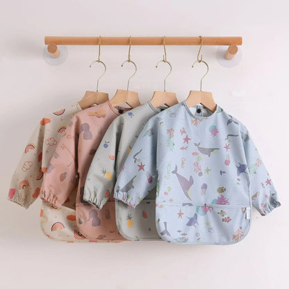Toddler in a blue long sleeve waterproof feeding bib enjoying a snack, keeping clothes clean