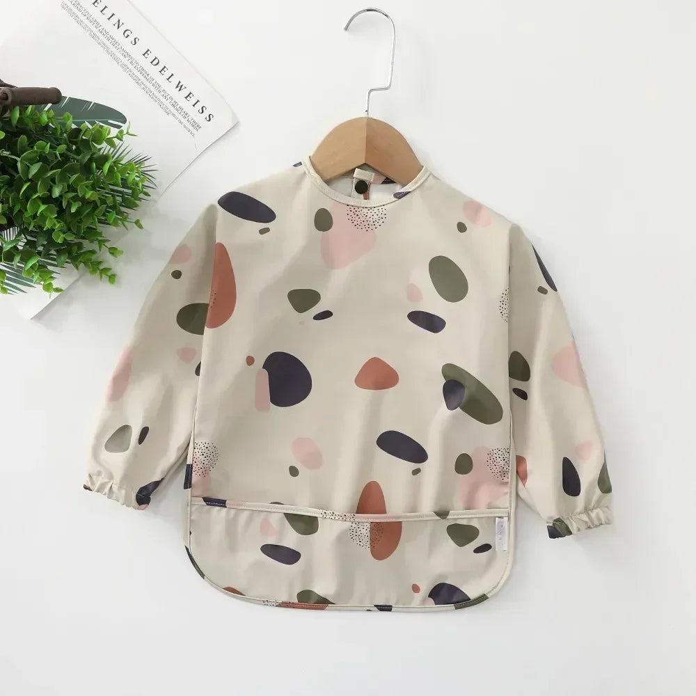 Long sleeve waterproof baby bib draped over a high chair, illustrating its practical use daily