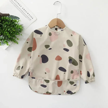 Long sleeve waterproof baby bib draped over a high chair, illustrating its practical use daily