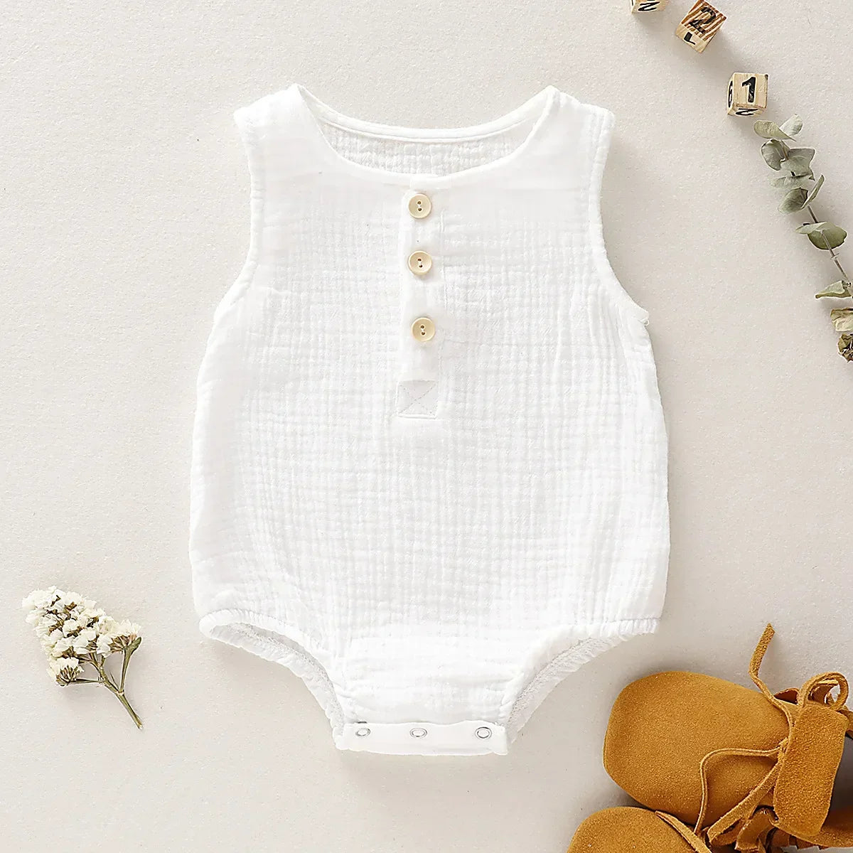 White muslin baby romper, a simple yet chic sleeveless jumpsuit for easy summer changing.