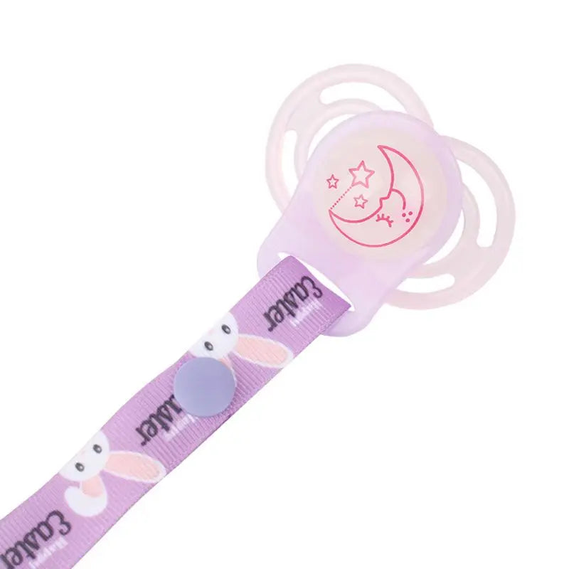 Baby's hand holding a pacifier attached to a secure pacifier clip with MAM ring adapter.