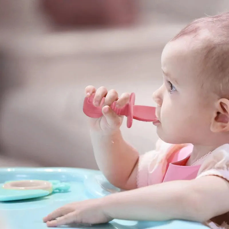 Toddler using a green silicone divided plate set with fork during baby led weaning mealtime