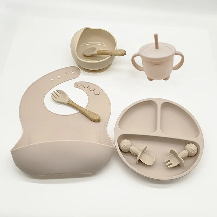Silicone mealtime solution for babies: suction plate, bowl, adjustable bib, & soft training spoon.