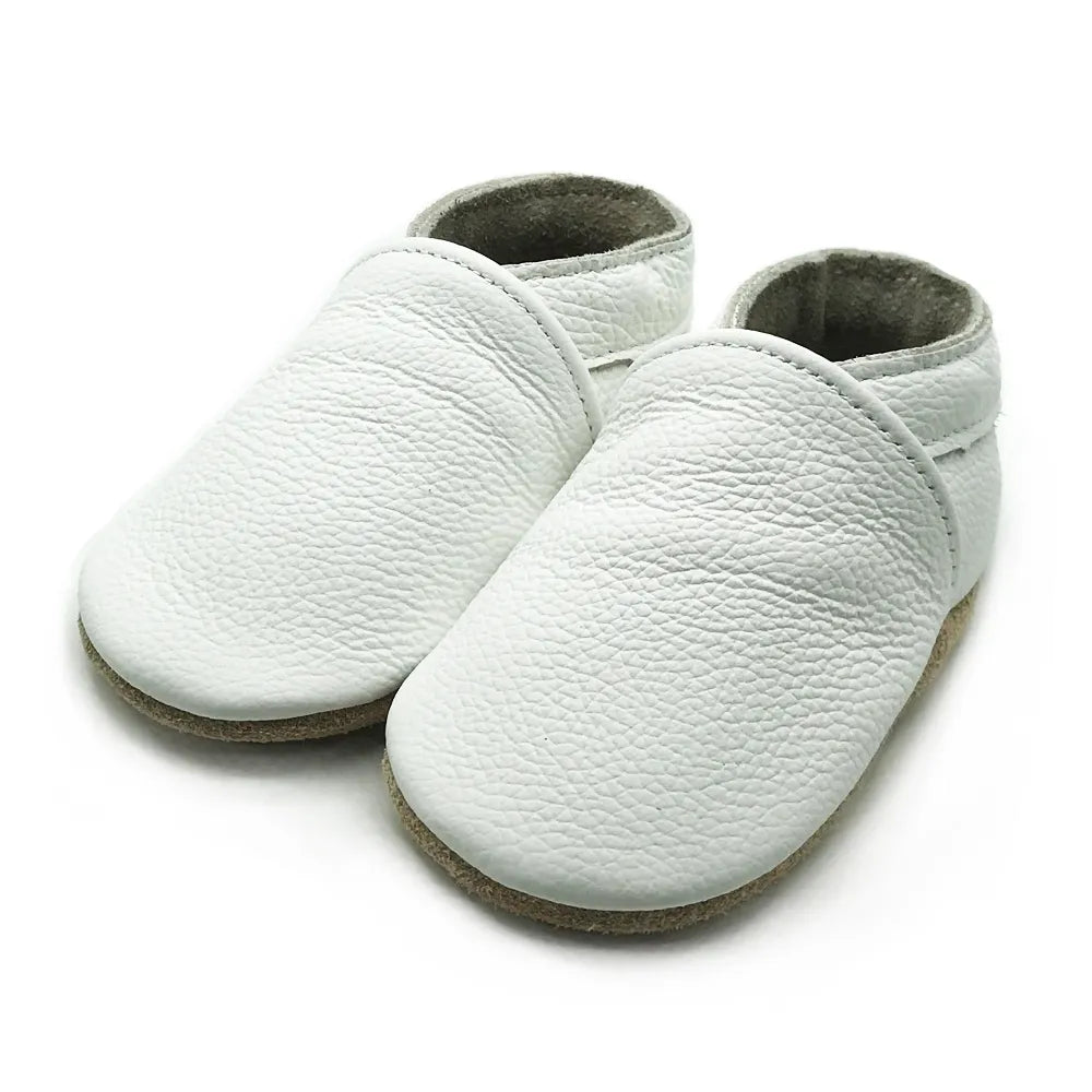 Infant taking first steps in white soft sole leather booties, unisex baby footwear