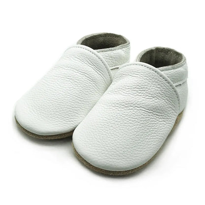 Infant taking first steps in white soft sole leather booties, unisex baby footwear