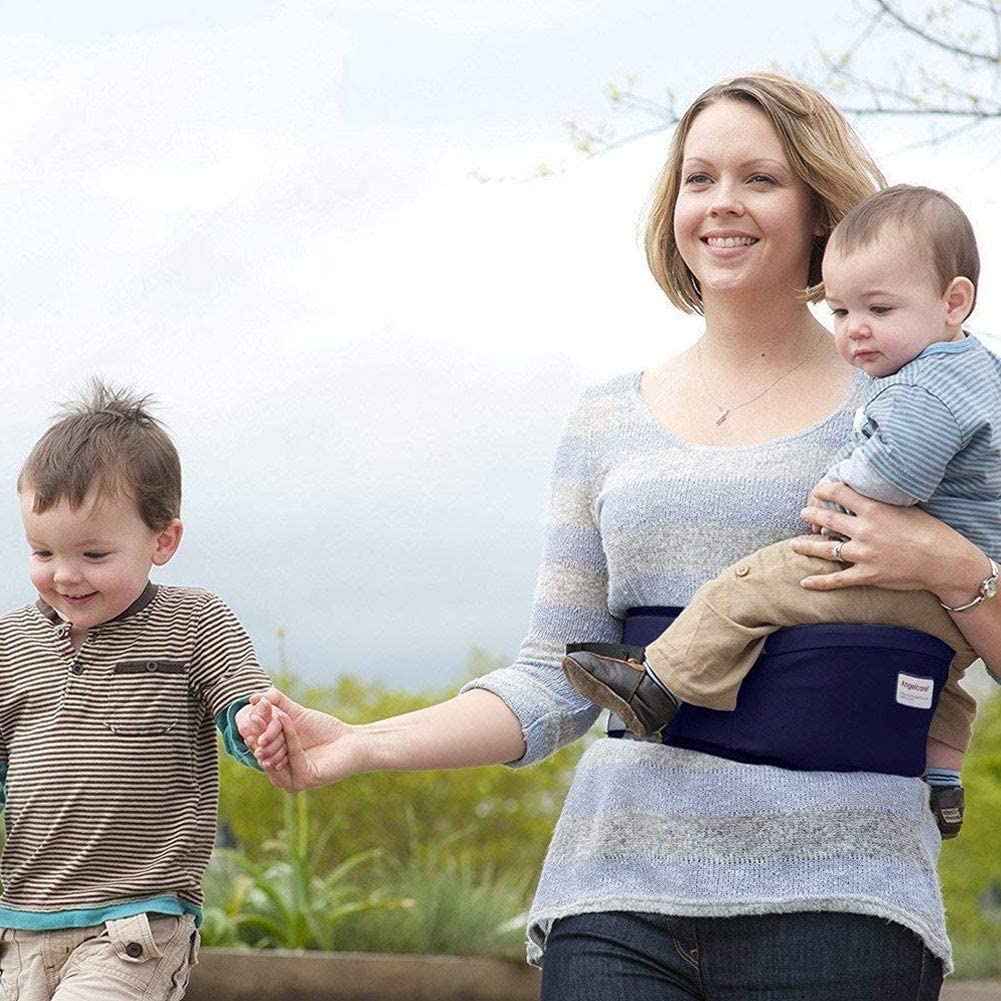 Parent carrying an infant in a beige ergonomic baby hip seat carrier, demonstrating ease of use