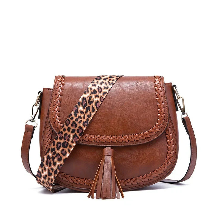 Side view of a chic women's brown saddle bag, featuring its unique curved shape and elegant tassel detail.