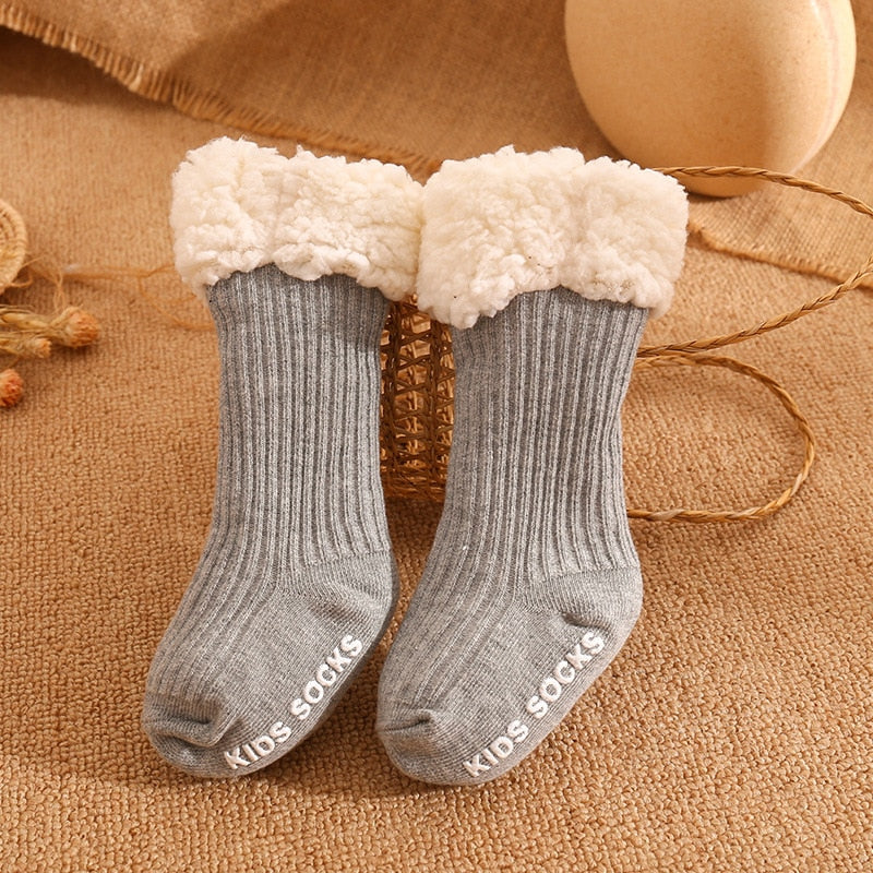 Infant feet in cozy, non-slip winter socks, peeking out from under a warm blanket