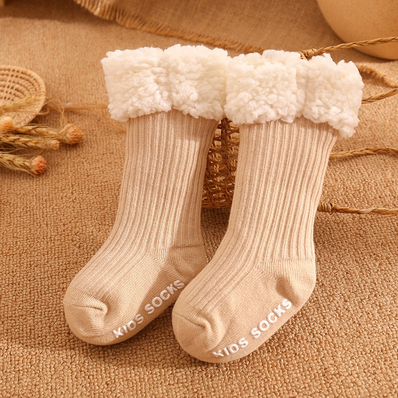 Toddler wearing a single thick, warm baby sock with non-slip grips on a wooden floor