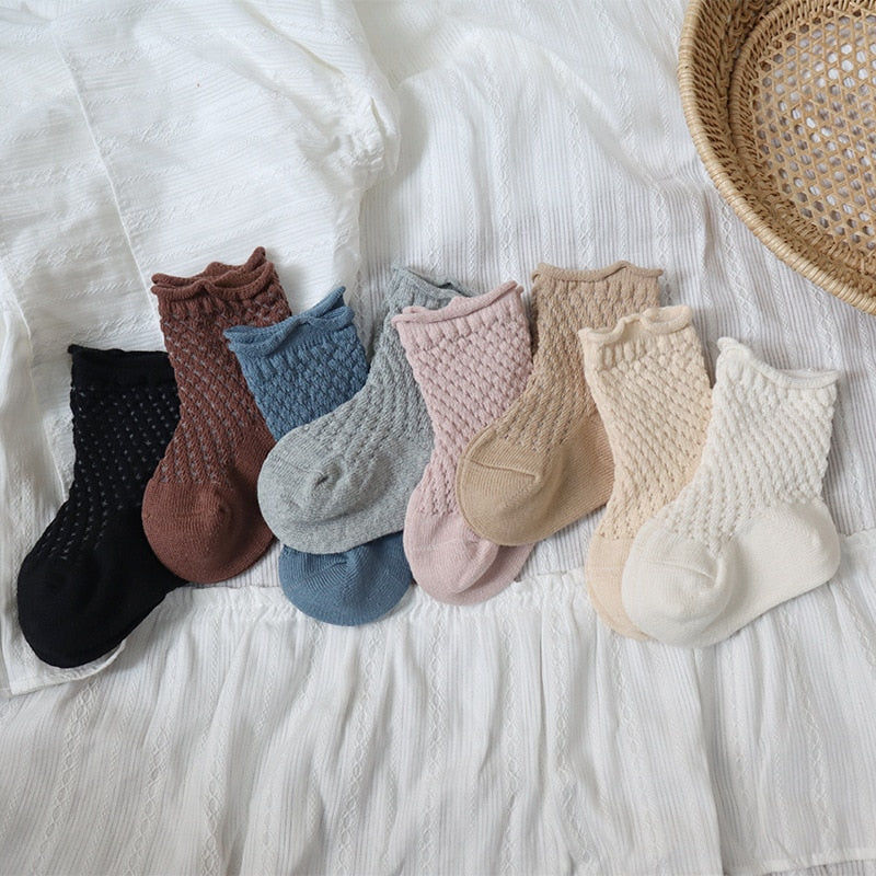 Close-up of a pair of white kids soft cotton mesh breathable ankle socks on a light surface.