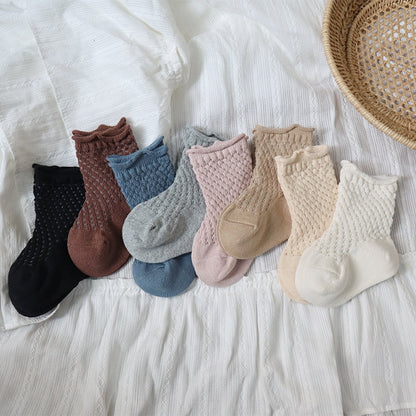 Close-up of a pair of white kids soft cotton mesh breathable ankle socks on a light surface.