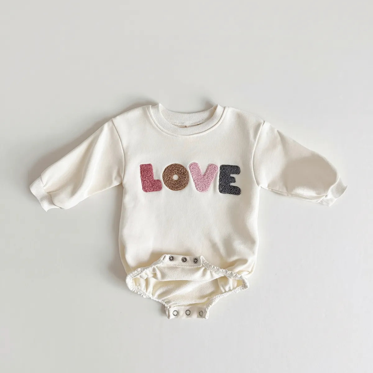 Cream baby romper on white background, highlighting its unisex design and 'love' detail.