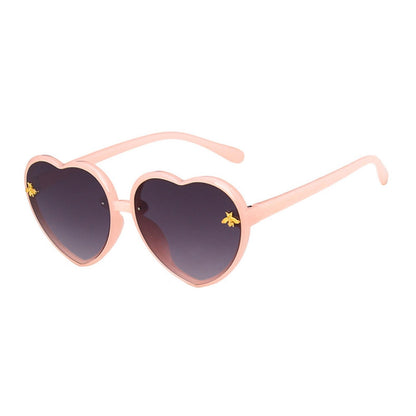 Child model playfully wearing heart-shaped green sunglasses, highlighting kids eyewear and summer essentials