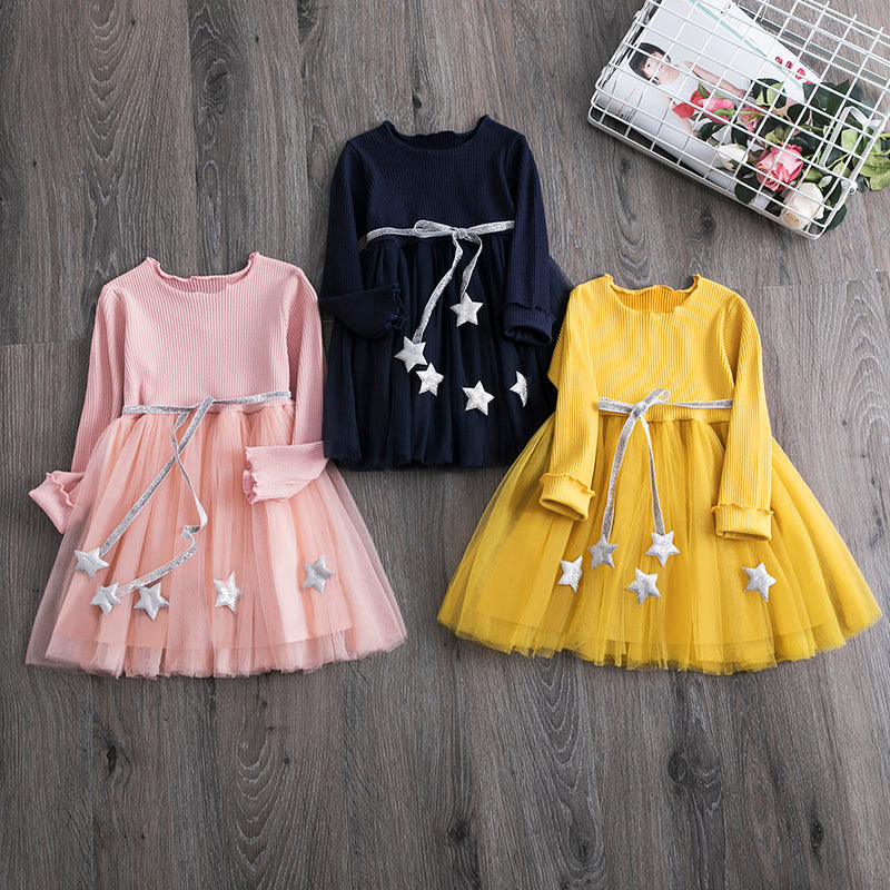 Young girl happily twirling in a stylish star mesh long sleeve party dress for toddlers.