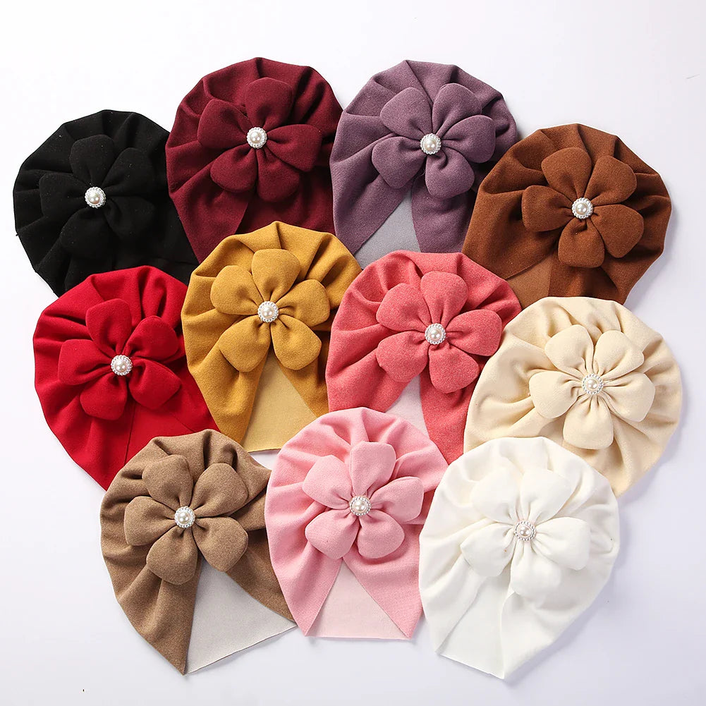 Elegant newborn turban hat in soft pink with pearl flower, perfect for baby girls.