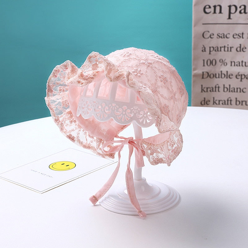 Newborn baby girl wearing a delicate white lace bonnet hat with floral embellishments.