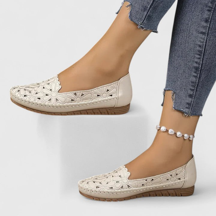 Close-up of women's beige ballet flats showcasing intricate perforated floral cutouts and scalloped trim.