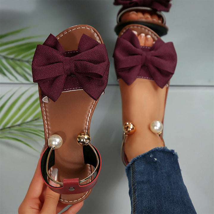 Elegant women's flat sandals, featuring decorative bow & bead accents. Comfortable summer vacation shoes.