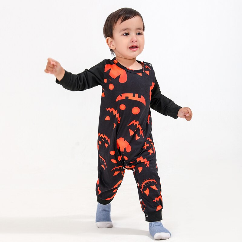 Toddler sitting on a rug in a cute Halloween monster print pajama, enjoying family matching sleepwear.