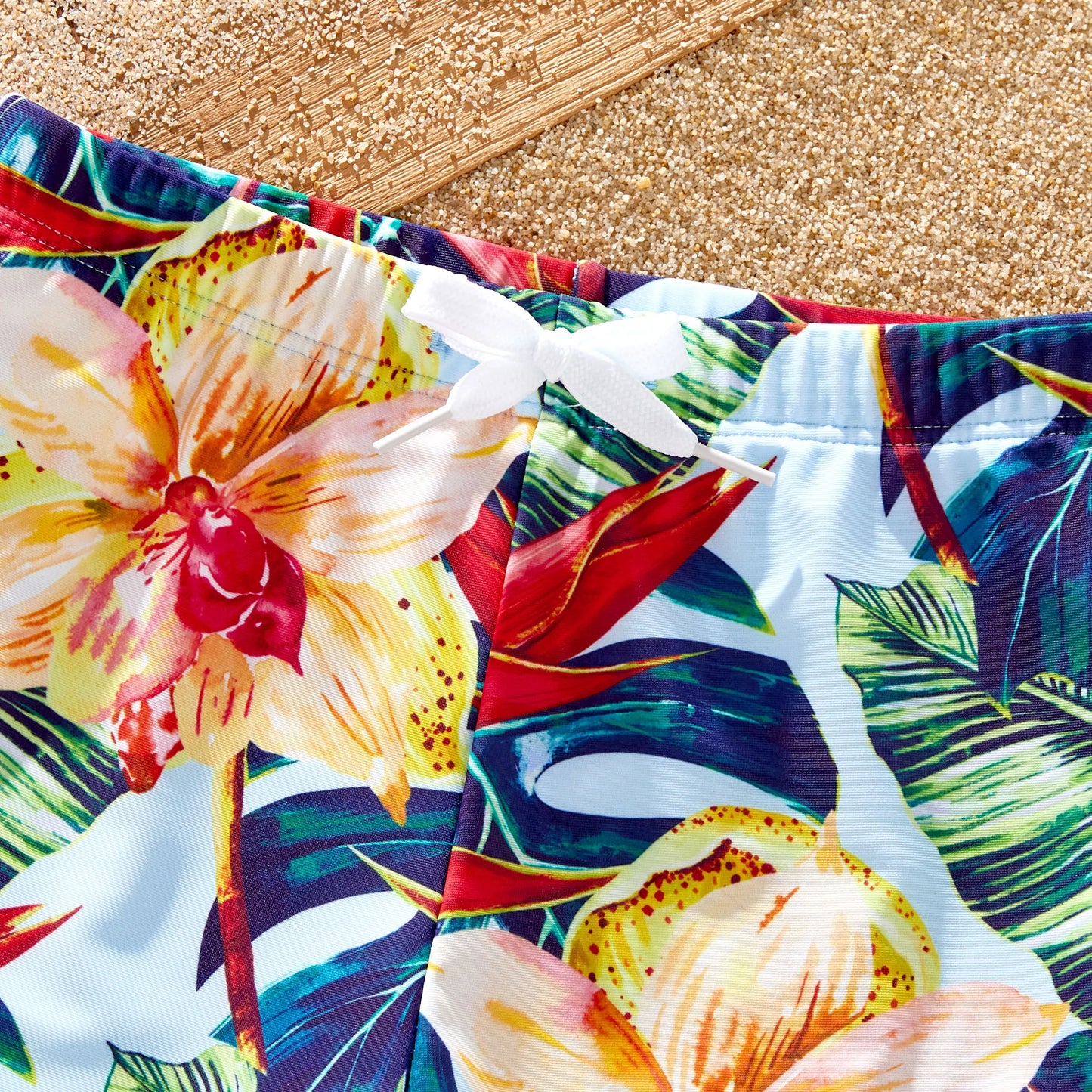 Family running on sand in matching floral swimsuits, ideal for beach vacation attire.