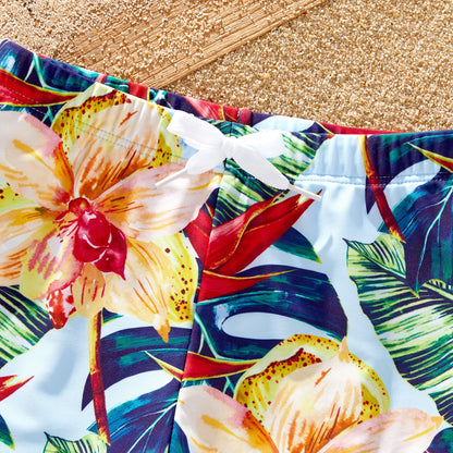 Family running on sand in matching floral swimsuits, ideal for beach vacation attire.