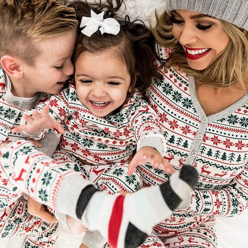 Mother and daughter in matching holiday pajamas, decorating a Christmas tree.